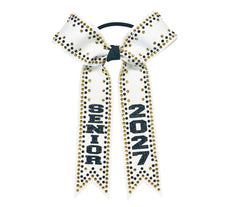 A white cheerleader hair bow with black and gold rhinestone accents, featuring the letters 'SENIOR' and 2027 in black glitter on one ribbon tail, attached to a black elastic band.