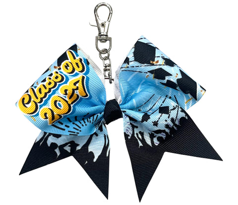 A cheerleader-style keychain bow with a silver clasp, featuring a light blue and black graduation-themed print with 'Class of 2027' text on one side.