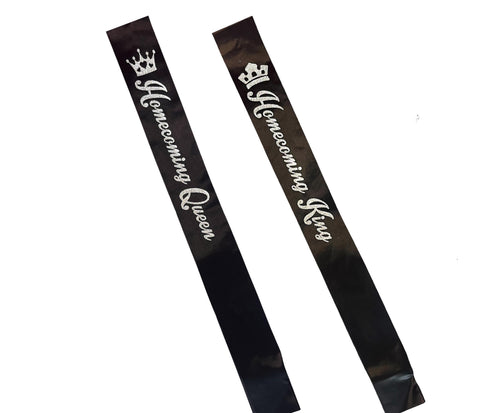 Two black satin homecoming sashes with white text and crown graphics, one reading 'Homecoming Queen' and the other 'Homecoming King', shown on a plain white background.