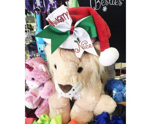 Stuffed lion wearing a Santa hat with 'Nasty' and 'Nice' bows, surrounded by other stuffed animals.