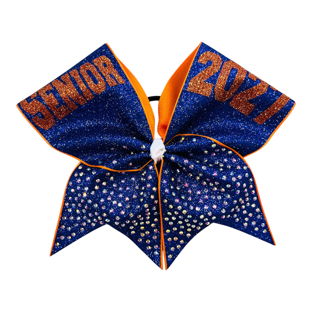 A cheerleader hair bow featuring a royal blue glitter top section with orange glitter text reading 'SENIOR' and '2027', and a lower section covered in small clear AB rhinestones, finished with orange trim.