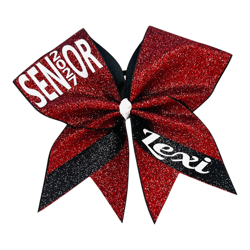 A cheerleader hair bow featuring a red and black glitter design, with 'SENIOR 2027' printed in white on one ribbon loop and 'Lexi' printed in white script on the other, set against a plain white background.